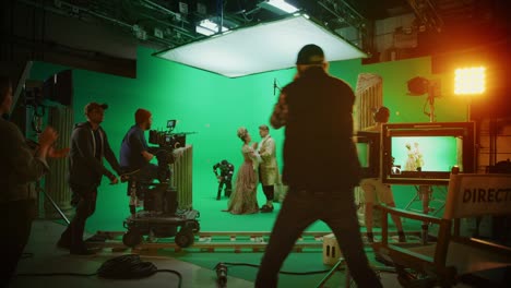 film studio set: shooting green screen scene with two talented actors wearing renaissance clothes talking, director finishes scene, celebrates success, embraces actors. period drama movie backstage