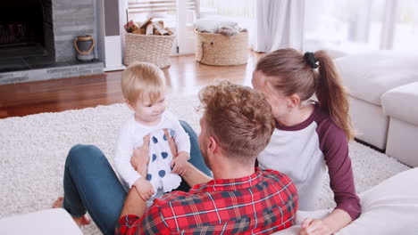 Junges-Paar-Hebt-Seine-Kleine-Tochter-Im-Wohnzimmer-Hoch