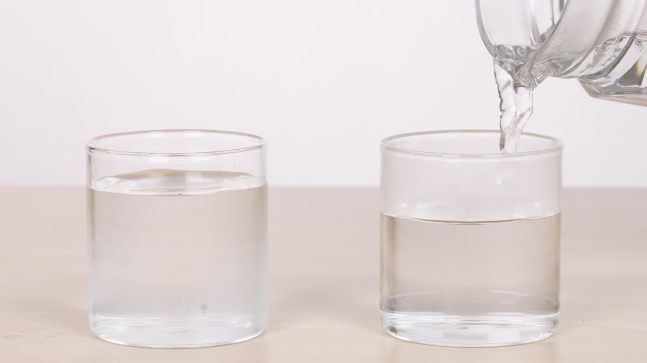 Clear water poured into glass on tabletop, neutral background, static camera, bright even lighting