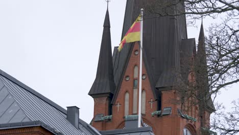 die flagge der schwedischen nationalkirche weht sanft auf einer stange und steht in der nähe eines skandinavischen gebäudes – weitwinkelaufnahme