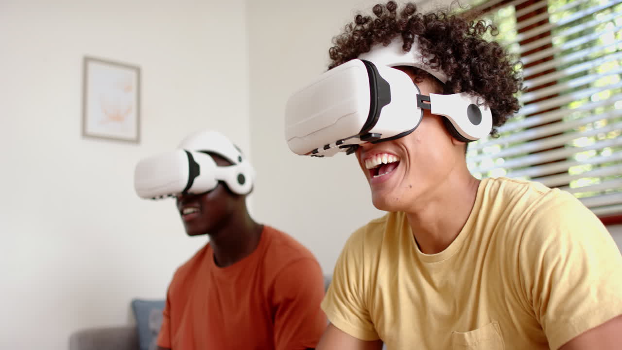 Wearing vr headsets, two multiracial male friends enjoying virtual reality experience, at home