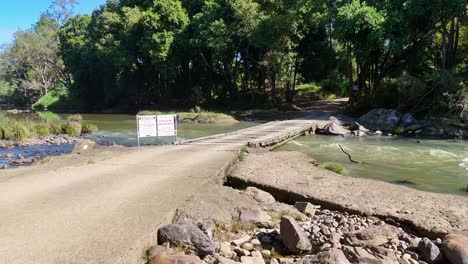 a dirt road crosses a creek with a private property sign. surrounded by lush greenery under bright daylight