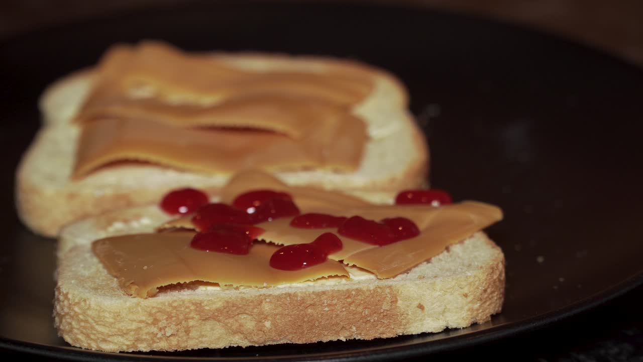 Putting strawberry jam on two slices of toast with brown cheese