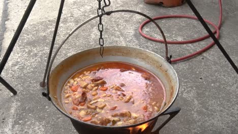 Leckere-Bohnen-In-Einem-Riesigen-Topf-über-Dem-Herd-Im-Freien-Kochen---Neben-Dem-Tisch-Aufgedeckt---Aufschlussreiche-Aufnahme