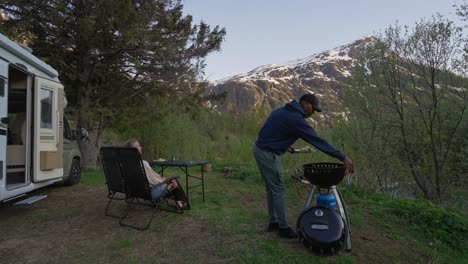 Couple camping free in nature of Norway while cooking dinner on BBQ