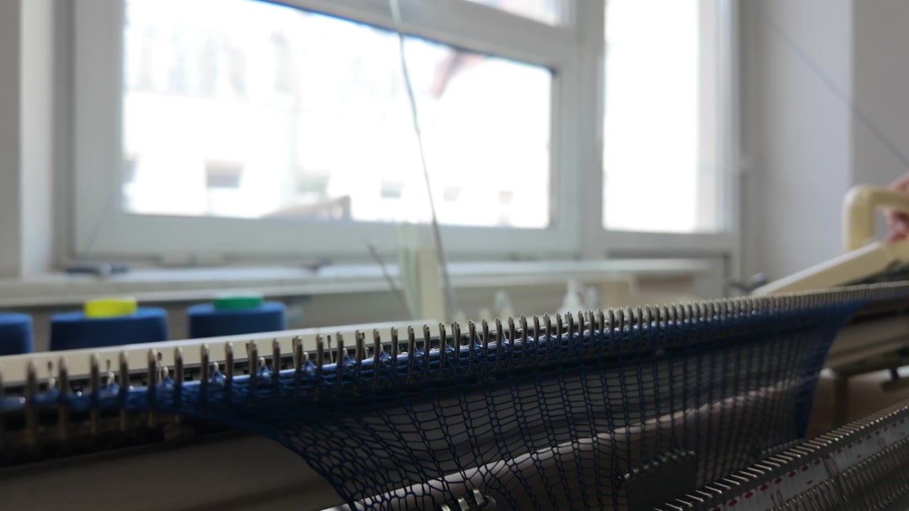 Detaljeret billede af blåt garn, der væves gennem en strikkemaskine, som viser interaktionen mellem tråde og metalnåle
