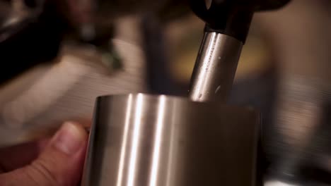 close-up of milk frothing in a stainless steel jug with steam wand, warm lighting, and steady camera