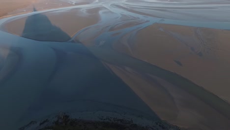 Drone-flying-near-statue-on-spire-of-Mont-Saint-Michel-abbey-and-view-of-bay