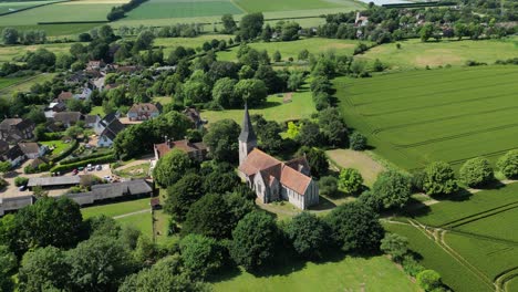 A-relaxed-aerial-push-in-shot-of-Ickham-village,-Kent,-with-St-John-the-Evangelist-church-and-surrounding-fields-clearly-visible