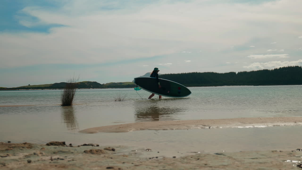 toma panorámica en cámara lenta de una niña poniendo una tabla de remos en un lago en el lago kai iwi, nueva zelanda