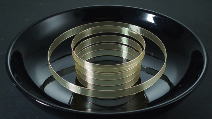 Tilting top band causing stacked gold bands sliding, flattening in black bowl, forming rings