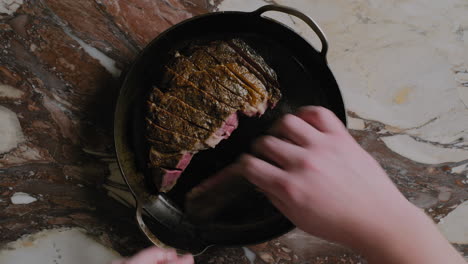 top-down shot of a ribeye steak being plated into a cast iron pan