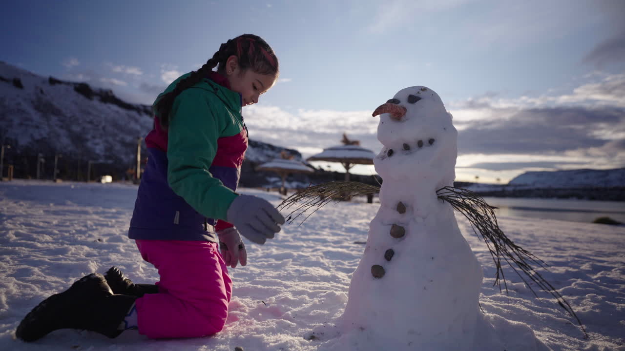 Young girl enjoying snowy day building snowman during family holiday trip
