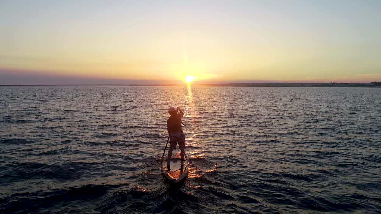 Paddleboarder chasing the sunset across a bay
