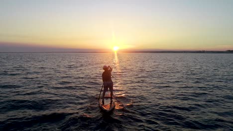 paddleboarder chasing the sunset across a bay