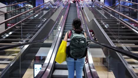 traveler ascending escalator at berlin airport, red installation overhead. tilt-up shot, modern ambiance