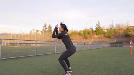 Mujer-Asiática-En-Ropa-De-Entrenamiento-Haciendo-Saltos-En-Cuclillas-Al-Aire-Libre