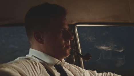 man smoking pipe in vintage car at night