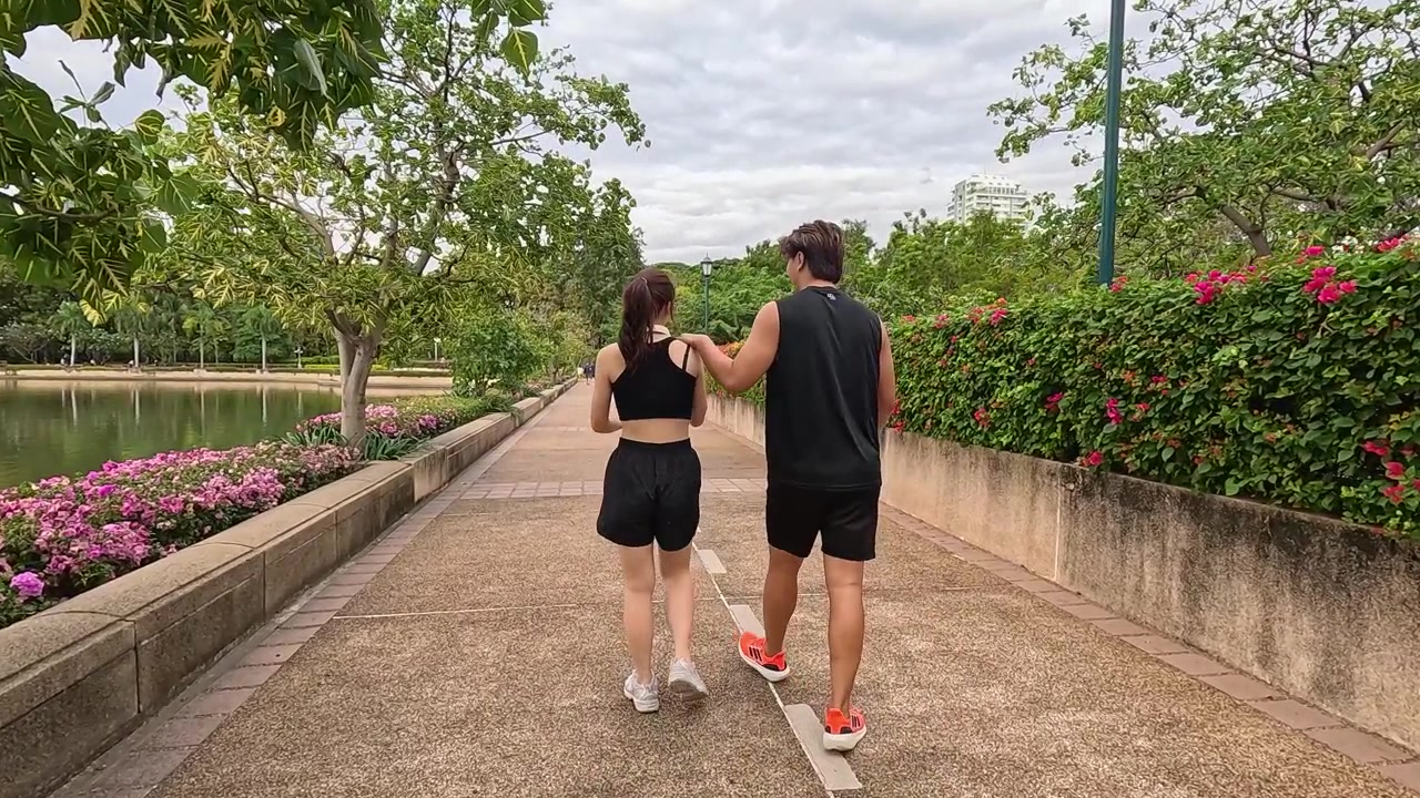 水辺の近くの公園の小道を一緒に歩く、健康的なカップルの後ろ姿。