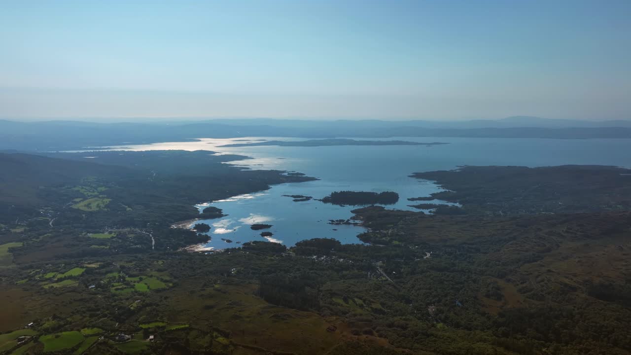 Caha Pass, County Cork, Ireland, September 2024. Drone tracks right with a panoramic overview of Glengarriff gliding above rolling lush green hills and farmland leading to the North Atlantic Ocean.
