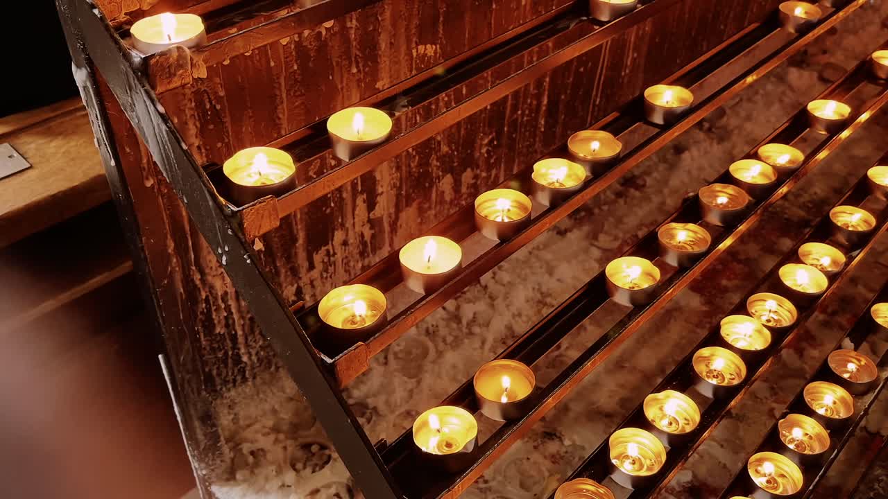 Ceri votivi dorati brillano su un supporto di metallo marrone all'interno di una chiesa di Vienna.