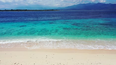 vivid colors of sea with blue turquoise lagoon and white waves washing sand of exotic beach on e bright summer day with cloudy sky in indonesia