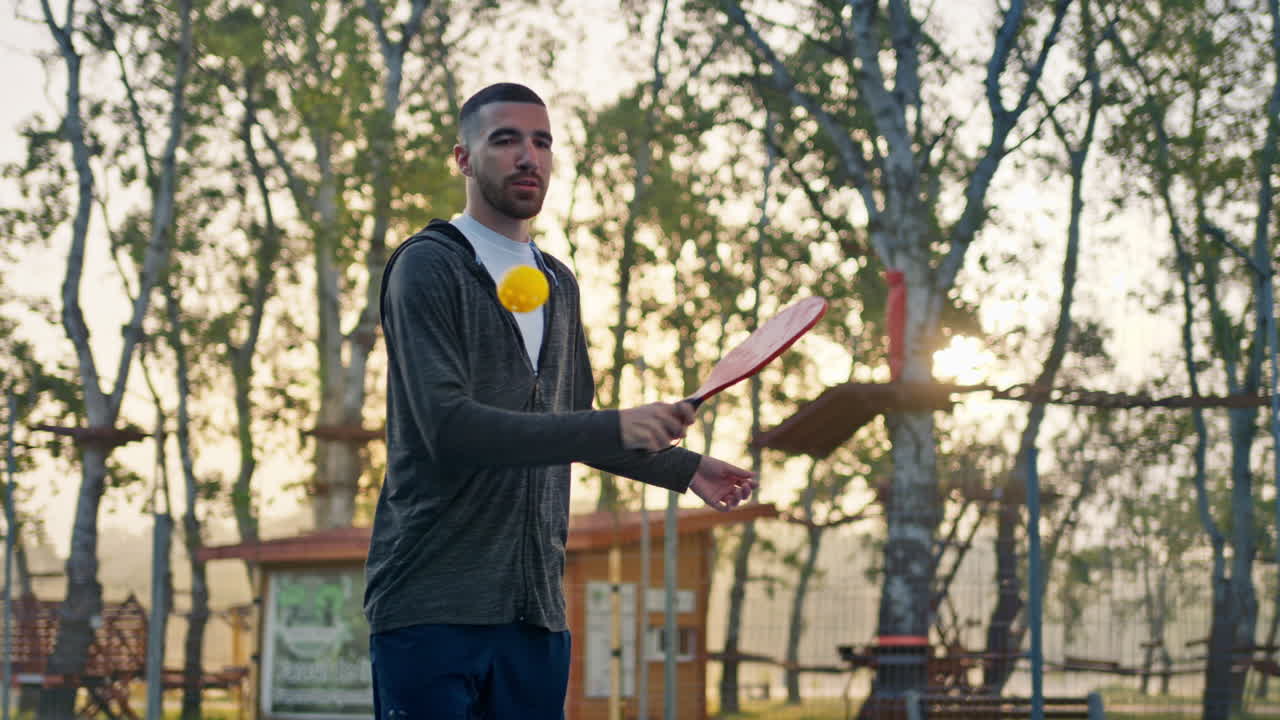 Man in zip up hoodie playing pickleball with a red racket after rain