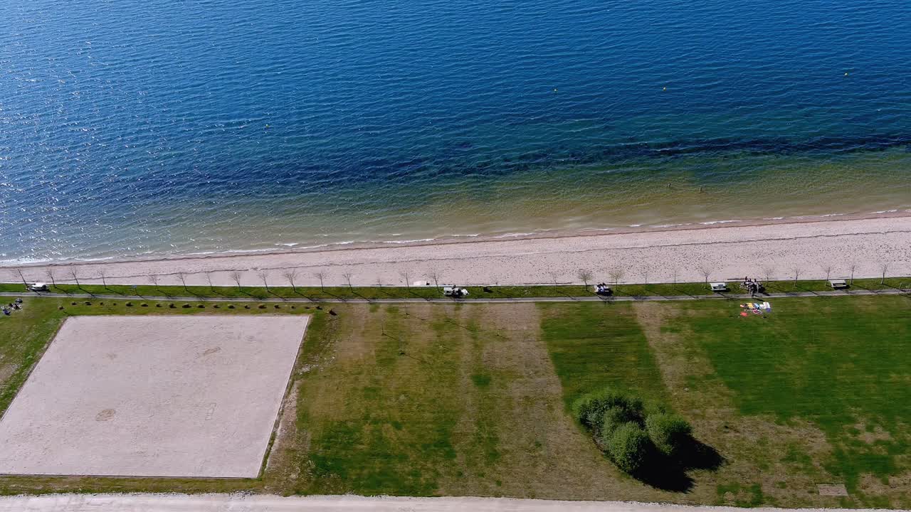 playa del lago con gente tomando el sol y bañándose, jardín y zona de paseo