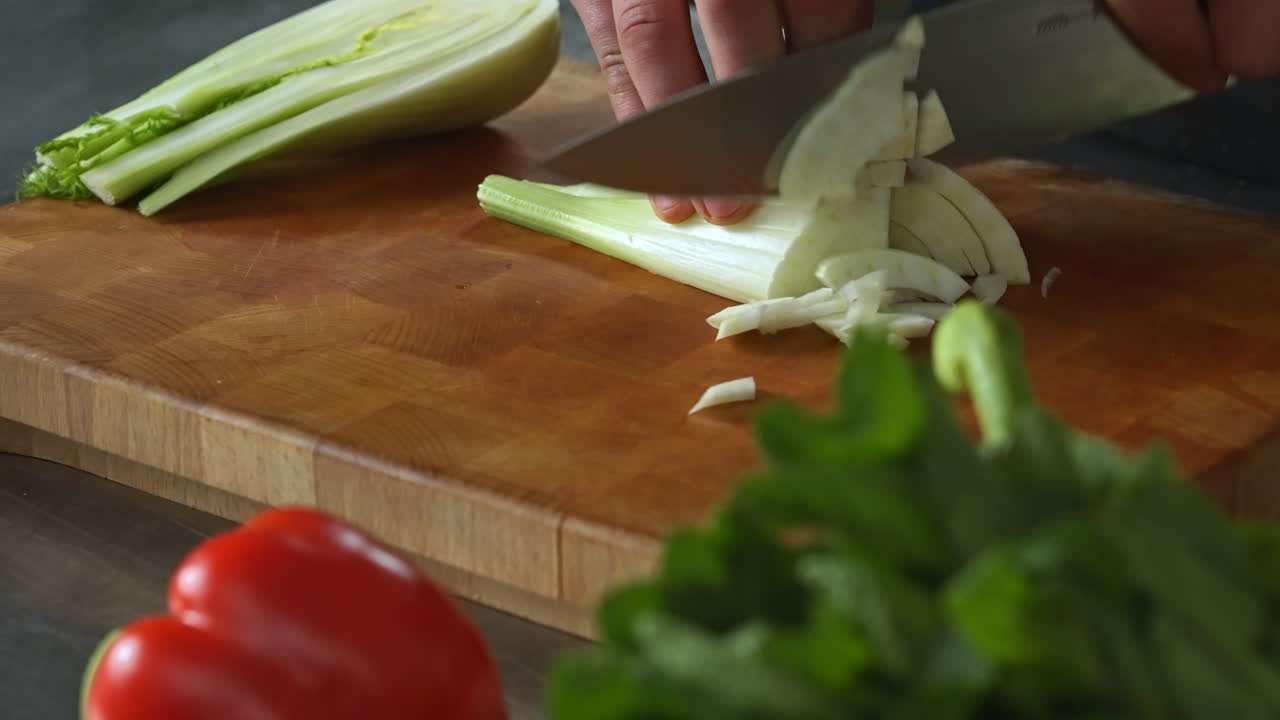 Chef slicing fennel on a chopping board with his left hand,vegetables