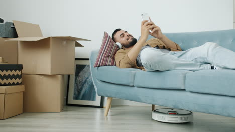 man relaxing on a couch with a robotic vacuum cleaner