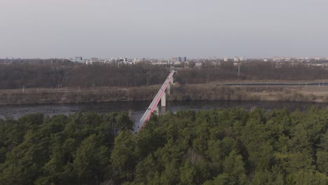 Un-Vuelo-De-Drone-Comienza-Sobre-Un-Denso-Bosque-Y-Avanza-Hacia-Un-Puente,-Revelando-Su-Envergadura-Completa-Mientras-Se-Conecta-Sobre-El-Río-Hacia-La-Ciudad.