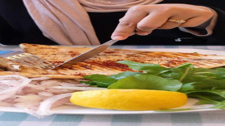Woman eating grilled fish with lemon and salad