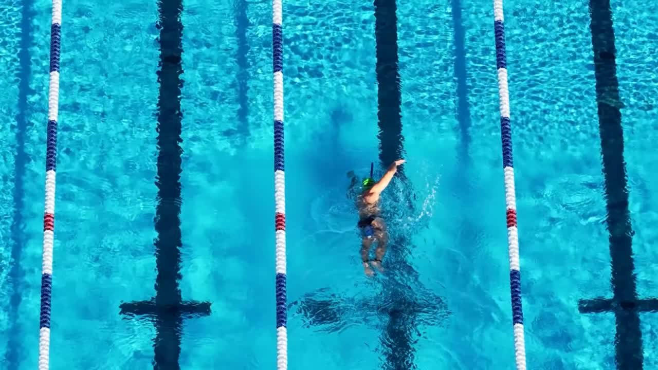 A top-down perspective of a male swimmer performing freestyle strokes in a sunlit lane