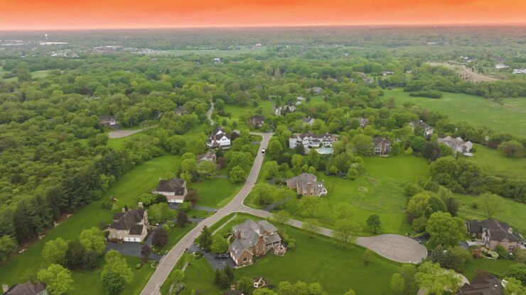 Well- kept suburban area in USA with beautiful private houses and neat roads. Rural neighborhood surrounded by green trees and grass lawns at the backdrop of orange sky.