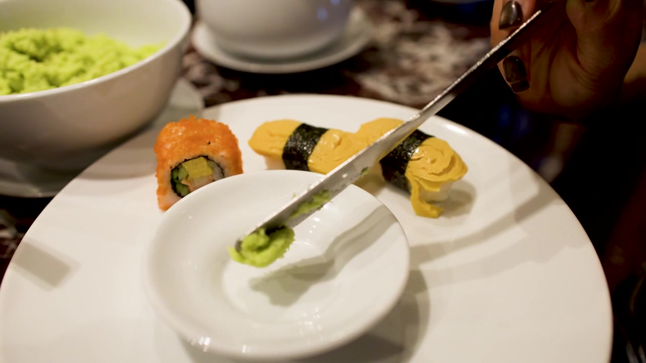 A person places a small dish and wasabi onto a plate with various sushi rolls