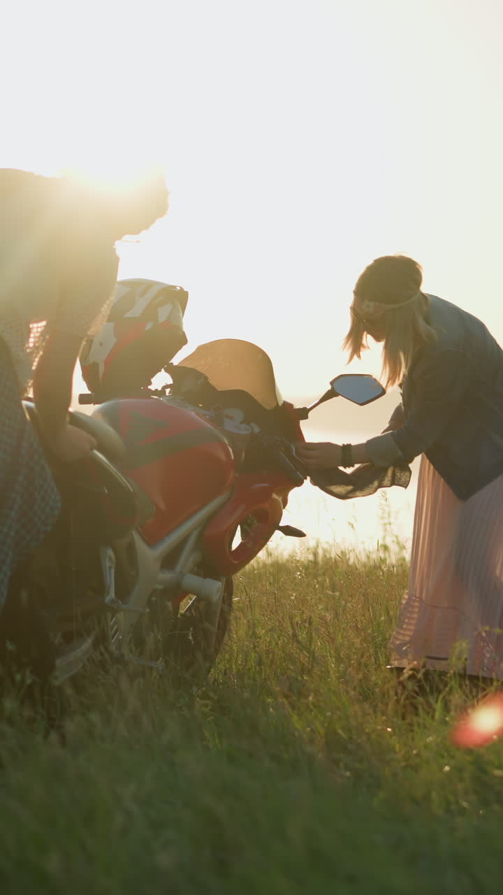 두 명의 여성이 은 모터사이클을 잔디에서 고 있으며, 태양은 다른 여인을 반영하고 있으며, 한 여성은 자전거 위에 구부려 있고, 다른 한 명은 조심스럽게 앞을 고 있습니다.