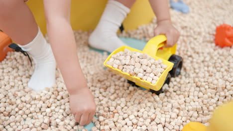 niño pequeño en la sala de juegos cargando el cubo de la excavadora con pequeños cubos de madera - manos close-up cámara lenta