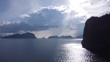 Vista-Aérea:-La-Luz-Del-Atardecer-Arroja-Sus-Sombras-Sobre-Una-Roca-Caliza-Alta,-Una-Nube-Hinchada-En-Un-Cielo-Despejado,-Un-Archipiélago-De-Pequeñas-Islas-De-Piedra-Caliza-En-El-Fondo