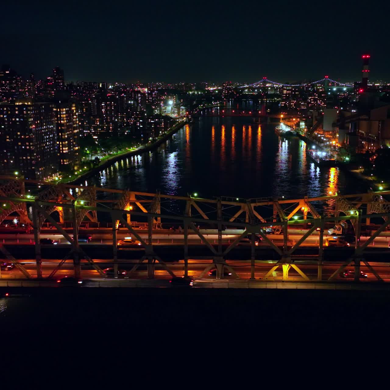 Multiple cars crossing the bridge at night. City lights reflecting in the river water. New York cityscape at backdrop