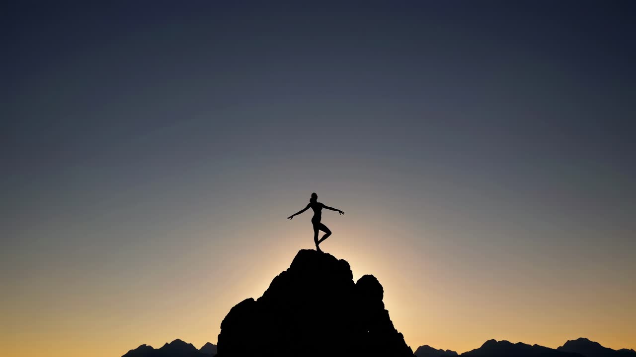 Silhouette di una persona in equilibrio su una cima di montagna al tramonto, ripresa da un'angolazione bassa