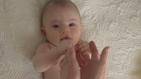 Fun-baby-portrait,-mom-playing-with-newborn-hands-arms-face-closeup,-white-bed-room