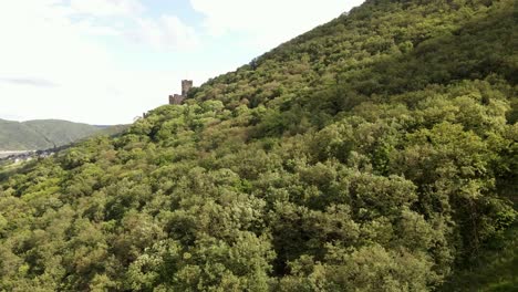 Antiguo-Castillo-Europeo-En-La-Ladera-Revelado-Detrás-De-Un-Exuberante-Bosque-Caducifolio-En-Un-Día-Soleado