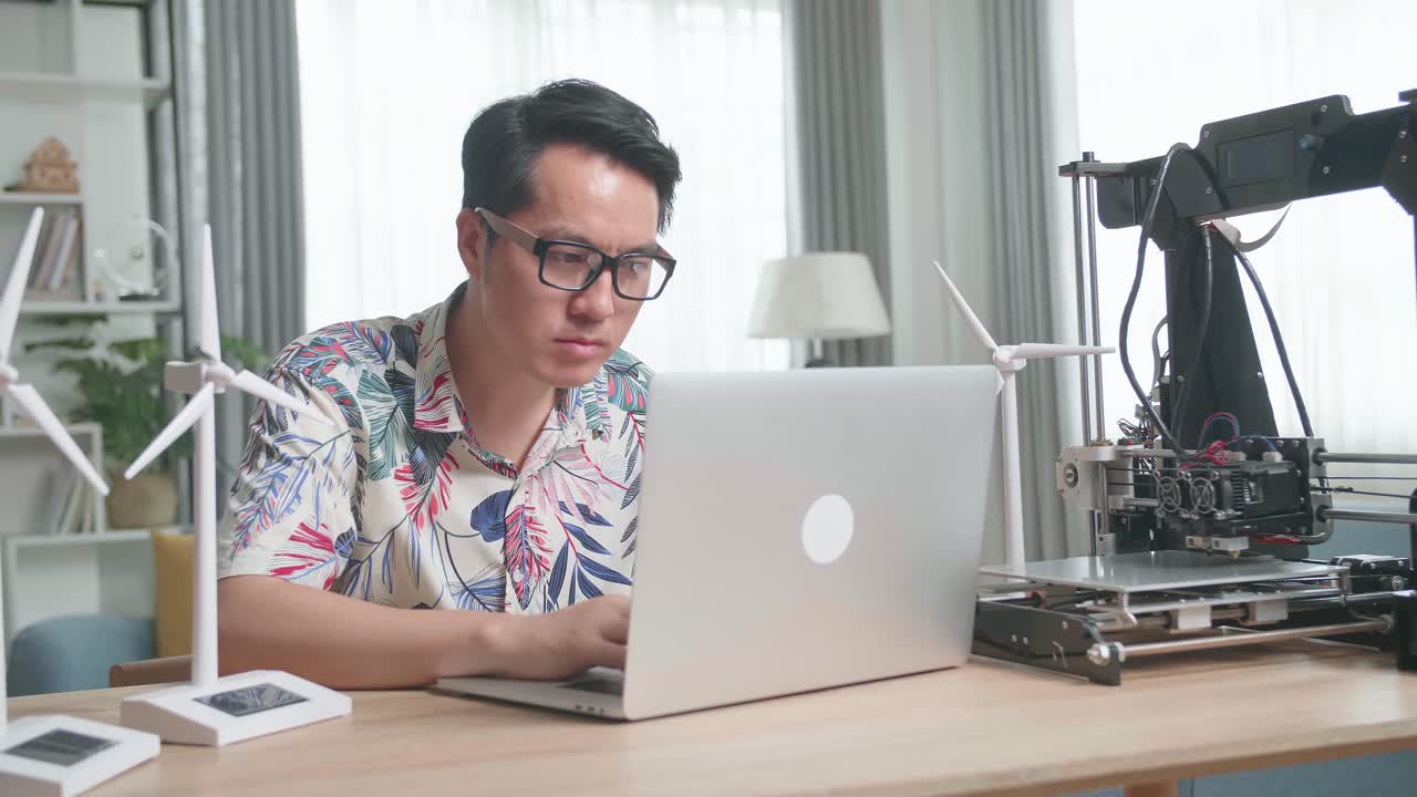 Man working on laptop with 3D printer and model wind turbines