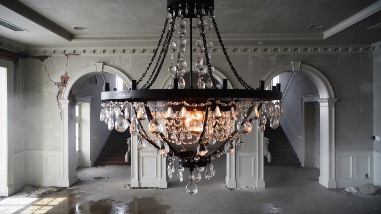 Grande lampadario di cristallo che oscilla, spostando la luce in un grande atrio su un pavimento bagnato a causa di un leggero movimento.
