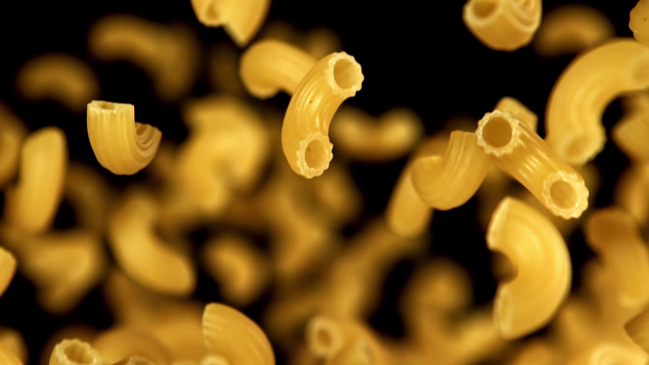 Pasta maccheroni secca che cade al rallentatore su sfondo nero.