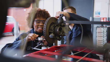 tutor with female students checking car brake discs on auto mechanic course at college