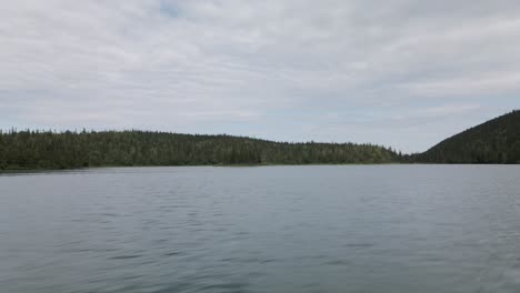 Overflying-The-Calm-Water-Of-The-Lost-Lake-With-A-Scenic-View-Green-Forest-And-Bright-Sky-At-Gaspesie-Peninsula,-Quebec,-Canada