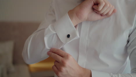 man in a white shirt adjusting his cufflinks, preparing for a formal event