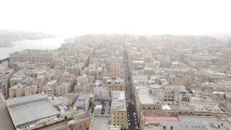 Drone-Vuela-Lateralmente-A-La-Derecha-Sobre-La-Calle-Principal-De-Malta-Con-Basílica-En-La-Neblina