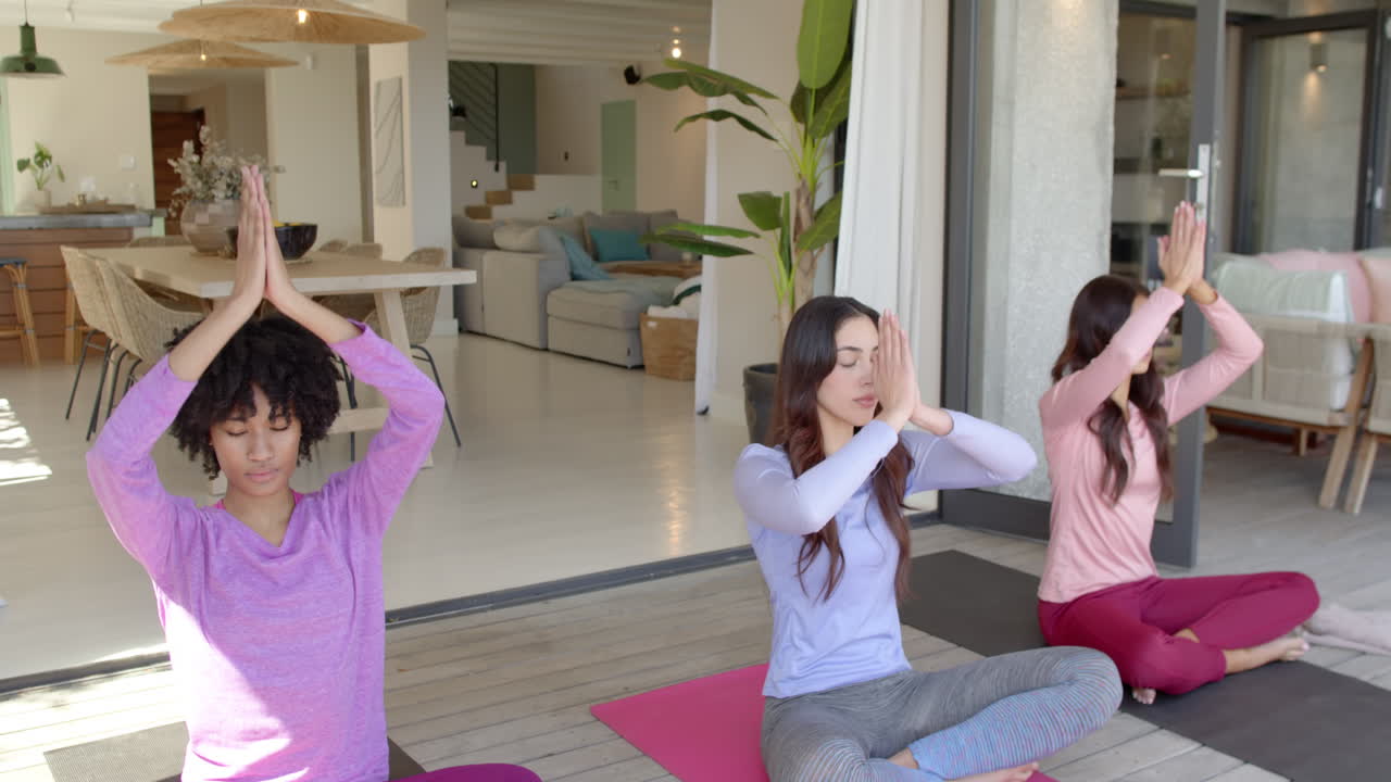 Women friends practicing yoga together at home, meditating on mats peacefully